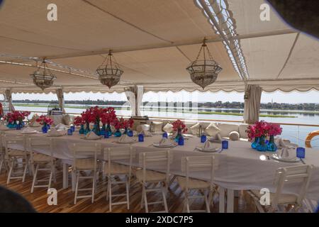 Bougainvillea-Blumen und blaue Glaswaren schmücken den Mittagstisch unter dem Baldachin auf dem Deck eines Dabahiya-Segelboots auf dem Nil, Ägypten. Stockfoto