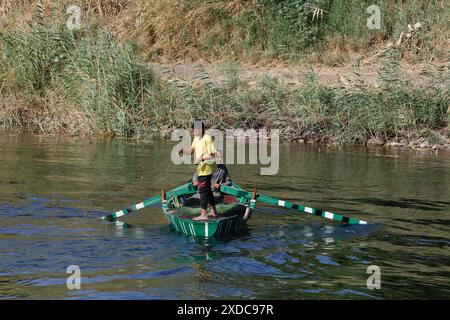 Ein traditionell gekleideter ägyptischer Mann rudert, während ein Junge in moderner Kleidung ein Fischernetz vom grünen Boot in das Wasser des Nils führt. Stockfoto