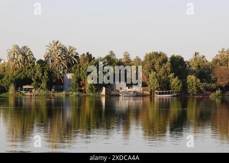 Eine Dorfwasseraufbereitungsanlage und zwei Flussfähren spiegeln sich in den Gewässern des Nils bei El-Kab, Ägypten, in der späten Nachmittagssonne. Stockfoto
