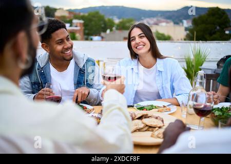 Junges, multirassisches, wunderschönes Paar, das am Tisch bei einem freundlichen Sommermahl im Freien sitzt. Stockfoto