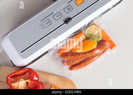 Vakuum-Lebensmittelversiegelungsmaschine, die einen Beutel mit gemischtem Gemüse und Würstchen auf einer Küchentheke versiegelt. Stockfoto