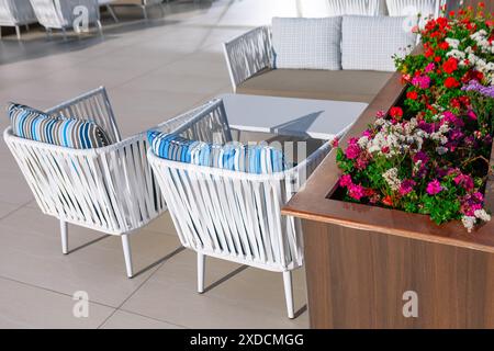 Terrassentisch und Stühle im Freien mit Blumendekoration in der Hotellobby. Restaurant-Terrasse mit weißem Tisch und Stühlen Stockfoto