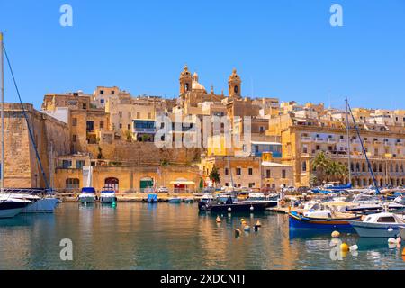 Die Altstadt von Senglea auf Malta. Das Wasser ist mit Booten verschiedener Größe gefüllt, darunter einige, die an einem Pier angedockt sind. Die Szene hat einen friedlichen und seh Stockfoto