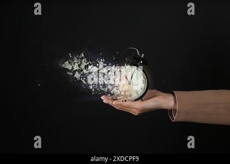 Geschäftsfrau mit auflösendem Wecker auf schwarzem Hintergrund, Nahaufnahme. Die Zeit läuft ab Stockfoto