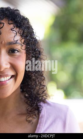 Lächelnde Frau mit lockigem Haar, die zu Hause Zeit genießt, mit hellrosa Hemd Stockfoto