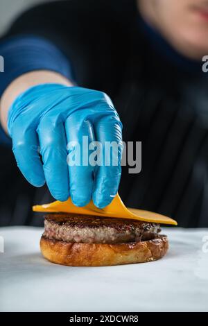 Der Restaurantkoch legt eine Scheibe Käse auf den Burger nahe. Stockfoto