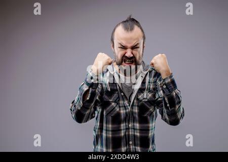 Ein aggressiver Mann mit Bart ballt seine Fäuste und zeigt seine Zähne in Wut. Er drückt negative Emotionen mit einer aggressiven Einstellung aus Stockfoto