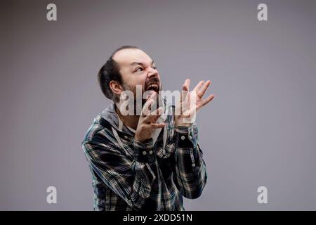 Bärtiger Mann schreit wütend, mit wilden Händen gestickt, zeigt Zeichen von Aggression und Stress in einem Porträt von intensiver Verärgerung und Wut Stockfoto