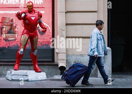 St. Petersburg, Russland. Juni 2024. Ein Mann mit einem Koffer geht an einer Statue des Marvel-Universums Iron man in St. Petersburg vorbei. Quelle: SOPA Images Limited/Alamy Live News Stockfoto