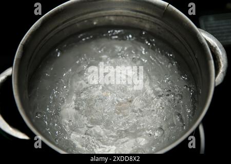 Ein mit kochendem Wasser gefüllter Edelstahltopf steht auf einem Gasherd. Dampf steigt aus dem Wasser auf und Blasen sind an der Oberfläche sichtbar Stockfoto