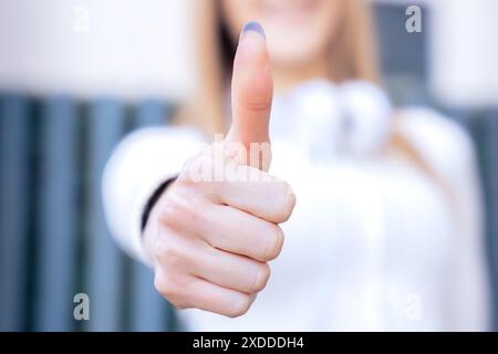 Unerkennbare junge Frau, die den Daumen nach oben zeigt und lächelnd in die Kamera schaut Stockfoto