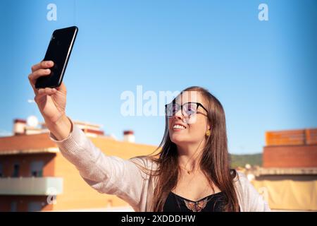 Junge kaukasische Frau, die ein Selfie mit Handy macht und draußen lächelt. Stockfoto