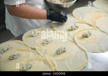 Der Arbeiter legt Fischfüllung auf runde Pfannkuchen Stockfoto