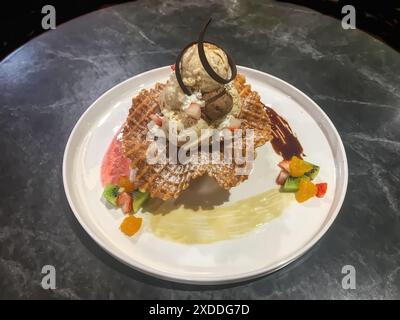 Köstliche Waffel mit Eis, Schokoladensirup, Erdbeersauce und frischem Obst auf weißem Teller. Stockfoto