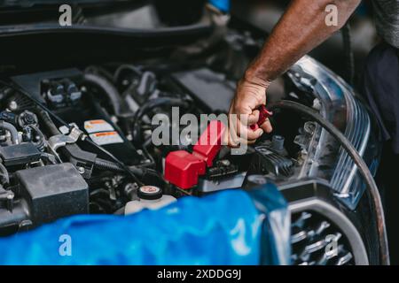 Nahaufnahme Mechaniker Handklemme Fahrzeugbatterieanschluss für Starthilfekontakku-Fahrzeug mit Niederspannungsbatterie in der Garage. Stockfoto