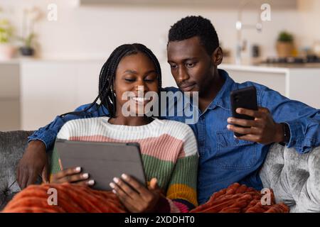 Das junge afroamerikanische Paar entspannt sich auf der Couch und genießt die sozialen Medien zu Hause Stockfoto