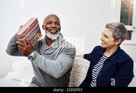 Überraschung, Sofa und reifes Paar mit Geschenk, um Geburtstag, Jubiläum oder Dankbarkeit zu Hause zu feiern. Liebe, glückliche Frau und Mann auf Sofa mit Geschenk Stockfoto