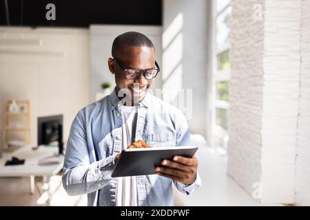Afrikanischer Geschäftsmann in schwarzem Anzug, der ein digitales Tablet in einem geschäftigen Markt für Online-Handel verwendet und Finanzen für globale Geschäfte verwaltet. Stockfoto