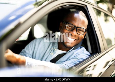 Der lächelnde Afroamerikaner verkörpert Erfolg, als er stolz sein neues Auto fährt und seine Fähigkeiten als CEO unter Beweis stellt. Stockfoto