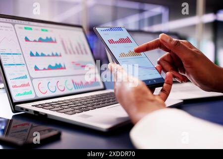 Die afrikanische Finanzberaterin verwendet ein KPI-Dashboard mit Analysediagrammen, um Börsentrends auf ihrem Laptop zu überwachen. Stockfoto