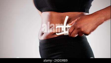 Afrikanische Frau mit einem Fettschieber zur Messung von Bauchfett, mit Schwerpunkt auf bariatrischer Gewichtsabnahme und Fettleibigkeit in der schwarzen Gemeinschaft. Stockfoto