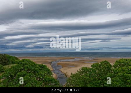 Die Mündung des Lunan River mündet in die Nordsee über die große Sandfläche, die bei Ebbe unter dunklen Sturmwolken freigelegt wird. Stockfoto