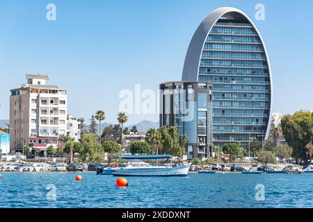 Motorboot, das am sonnigen Sommertag an einem modernen, ovalen Wolkenkratzer in Limassol Zypern vorbeifährt Stockfoto