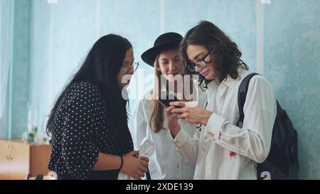 Drei High School-Schüler diskutieren etwas auf einem Smartphone. Stockfoto