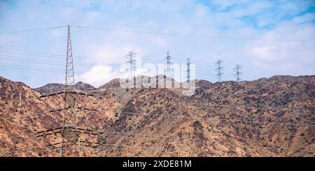 Medina, Saudi-Arabien - 22. Dezember 2022: Hochspannungsleitungen dominieren die trockene Landschaft vor dem Hintergrund zerklüfteter Berge. Stockfoto