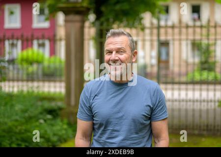 Ein reifer Mann mit blauem Hemd steht draußen mit einem Lächeln. Stockfoto