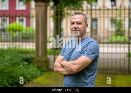 Ein reifer Mann mit blauem Hemd steht draußen mit überkreuzten Armen und strahlt Selbstvertrauen aus Stockfoto