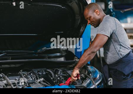 Garagenmechaniker African Black männlich professionell arbeitende Auto Service Ladebatterie. Batterie Wird Geprüft. Stockfoto