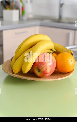 Reife saftige Früchte auf einem Holzteller auf dem Küchentisch. Küchenutensilien im Hintergrund. Stockfoto