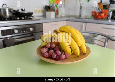Reife saftige Früchte auf einem Holzteller auf dem Küchentisch. Küchenutensilien im Hintergrund. Stockfoto