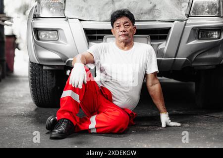 Portrait-Automechaniker, der in der Werkstatt für Autowerkstätten arbeitet. Erwachsener Arbeiter sitzt mit altem Auto. Stockfoto