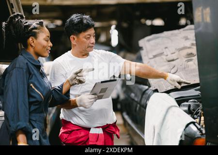 Reifer erfahrener Mechaniker, der junge Teenager-Arbeiterinnen ausbildet, um das Servicefahrzeug mit Tablet-Technologie zu überprüfen. Stockfoto