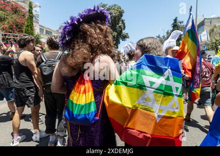 Haifa, Israel 21. Juni 2024, Pride Parade. Zwei Leute von hinten gesehen, das Mädchen ist in eine Regenbogenfahne gewickelt, der Mann trägt einen Rucksack mit Regen Stockfoto