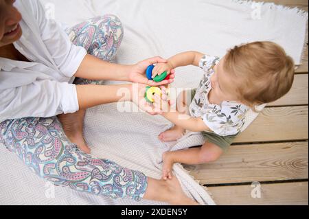 Mutter und Kind sitzen auf einer Decke, spielen spielerisch mit farbenfrohen Spielzeugen und fördern die Bindung und Kreativität. Stockfoto