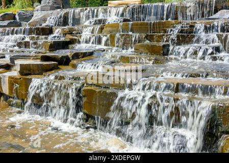 Nahaufnahme von Steinstufen eines künstlich geschaffenen Wasserfalls, Wasser fließt auf Steintreppen. Spaziergang im Park. Stockfoto