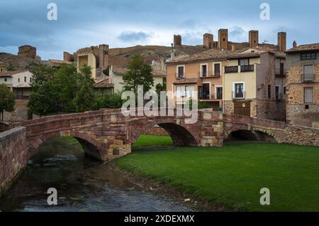 Blick auf eine mittelalterliche Brücke mit rötlichen Steinblöcken und die Burg auf der Spitze des Hügels an einem bewölkten Tag, Molina de Aragon, Guadalajara, Spanien Stockfoto