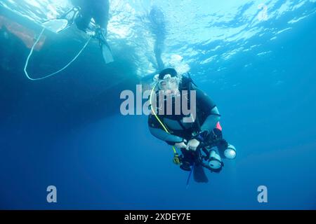 Ein Taucher mit einer Kamera schwimmt unter Wasser neben einem Boot an der Oberfläche. Tauchplatz Meeresschutzgebiet Cap de Creus, Rosas, Costa Brava, Spanien, Mittelmeer Stockfoto