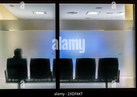 Silhouette eines Mannes, der allein in einem leeren Wartezimmer des Krankenhauses hinter Milchglas sitzt und ein Gefühl der Einsamkeit schafft. Stockfoto