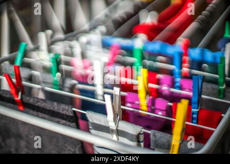 Nahaufnahme von farbenfrohen Kleiderschalen, die verschiedene Kleidungsstücke auf einem Wäscheständer sichern. Lebendige Kleidung, die drinnen trocknet, mit weichem Hintergrund. Stockfoto