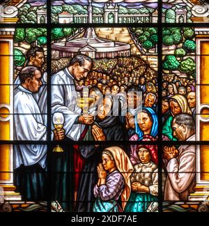 Ein Priester, der die Kommunion an die Gläubigen verteilt. Ein Buntglasfenster in der Basilika unserer Lieben Frau vom Rosenkranz in Fatima, Portugal. Stockfoto