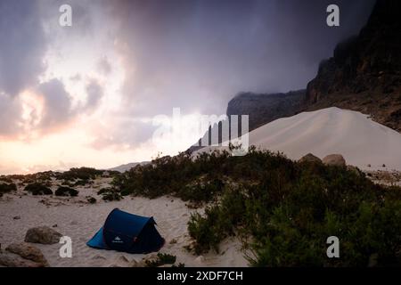 Atemberaubende Aussicht auf den Sonnenuntergang am Arher Beach, Socotra, Jemen, mit einem einsamen Campingzelt vor dem Hintergrund majestätischer Sanddünen und zerklüfteter Berge. Stockfoto
