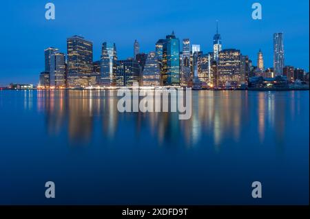 Sonnenaufgang über Manhattan von Brooklyn, lange Exposition mit den Lichtern der hohen Gebäude, die im blauen Morgenlicht reflektiert werden. Stockfoto