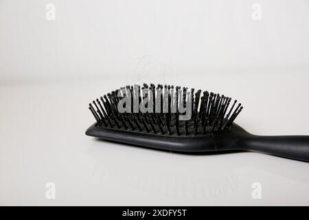 Nahaufnahme einer benutzten schmutzigen Haarbürste voller Haare auf weißem Tisch, Haarausfall-Problem-Konzept Stockfoto