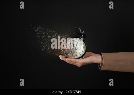 Geschäftsfrau mit auflösendem Wecker auf schwarzem Hintergrund, Nahaufnahme. Die Zeit läuft ab Stockfoto