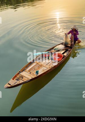 Hoi an (Hoian), Vietnam - 12. April 2018: Fantastischer Blick auf die vietnamesische Frau in traditionellem Bambushut auf einem Holzboot, das ihr Fischernetz überprüft. Stockfoto