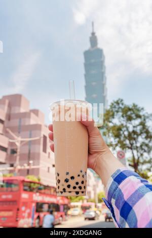 Nahaufnahme der weiblichen Hand mit traditionellem taiwanesischen Bubble Milk Tee in der Innenstadt von Taipei, Taiwan. Der Wolkenkratzer ist im Hintergrund sichtbar. Stockfoto